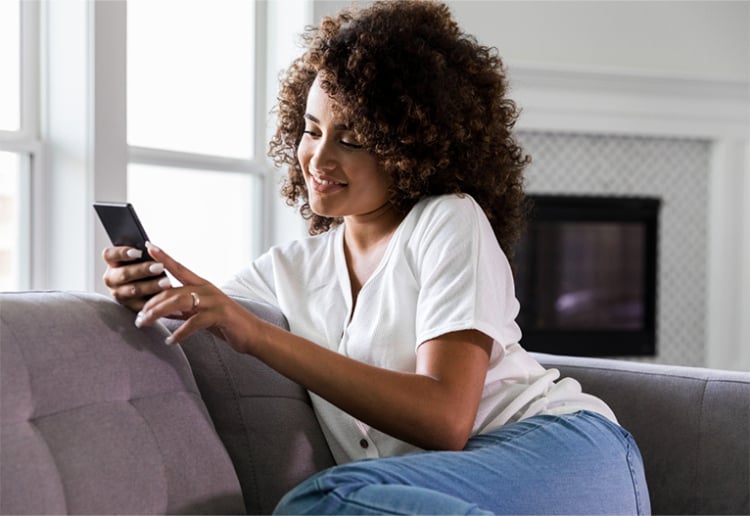 Woman using phone on a grey sofa.