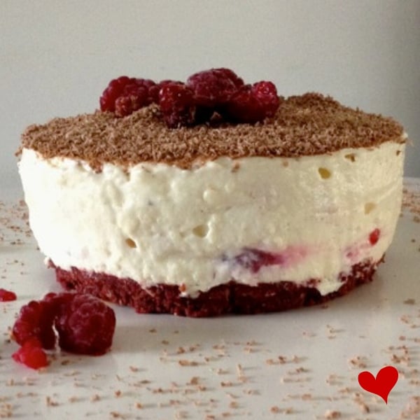 Individual sized white chocolate cheesecake with a red velvet tim tam base topped with grated chocolate and raspberries