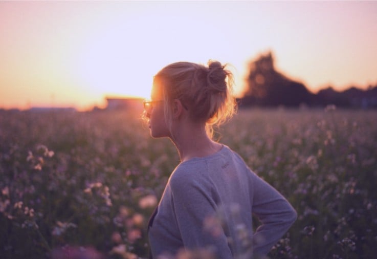 sunset photo of lovely blonde woman in a field of flowers with trees in the background