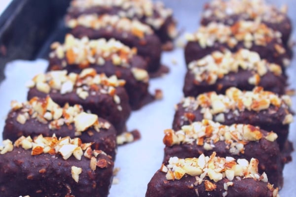 chocolate coated bars sprinkled with chopped almonds sitting on baking paper on a baking tray