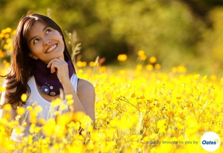 Beautiful woman in field of fresh yellow flowers looking up with her finger on her chin