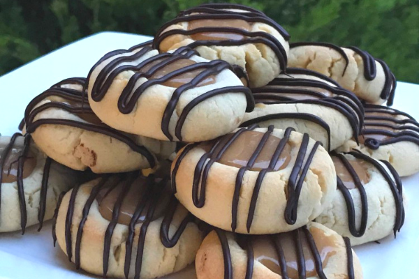 Small round biscuits served on a white platter with a caramel centre and drizzled with dark melted chocolate