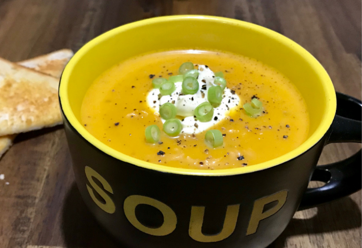 Black Soup Bowl filled with golden carrot pumpkin and ginger soup topped with a dollop of sour cream and spring onions