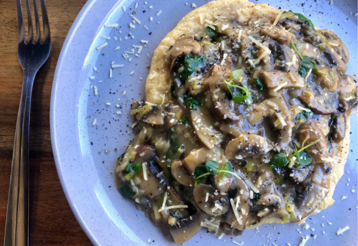 Blue plate on wooden bench with creamy polenta topped with a deliciously rich Mushroom Ragout