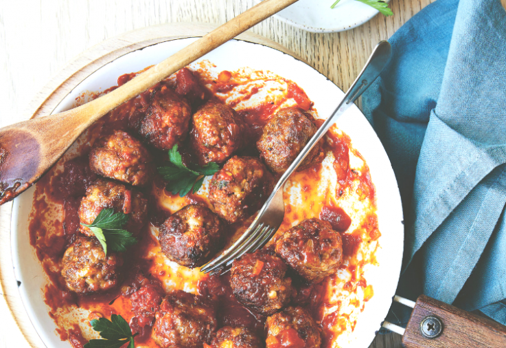 Large white plate filled with delicious lamb and haloumi meatballs in a chermoula based tomato sauce on a timber table with blue napkin