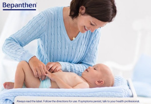 Bepanthen Nappy Rash Ointment being used at nappy change time by a mum in a blue sweater with her baby