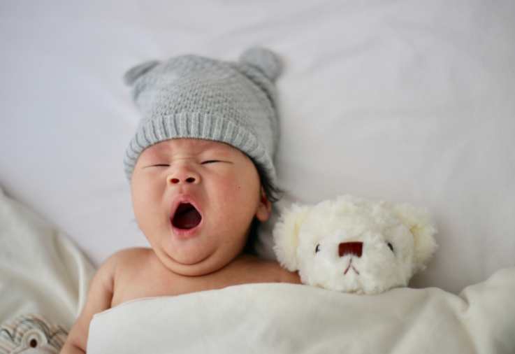 A cute baby with yawning in bed next to their teddy inspires unisex names