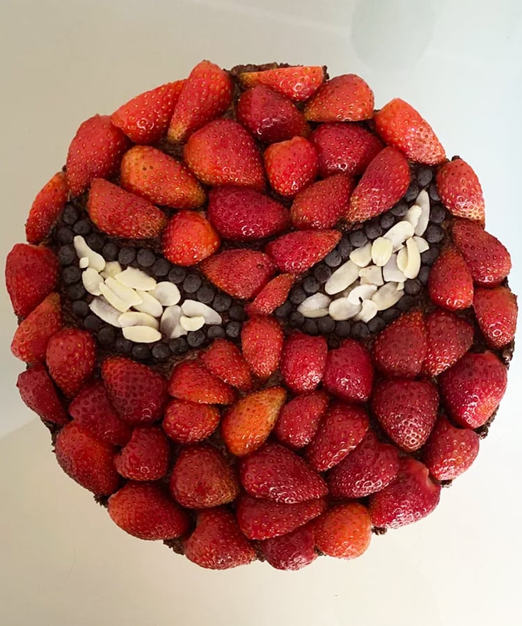 Kids round superhero birthday cake covered in strawberries.
