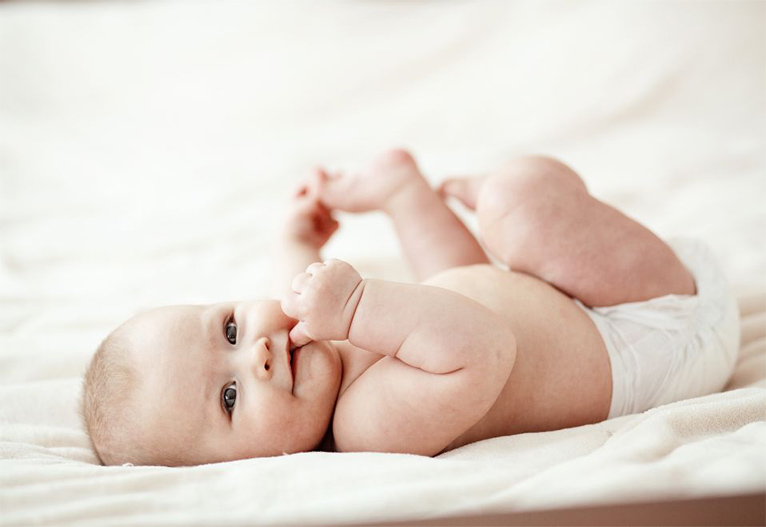 A baby lying on a bed smiling.