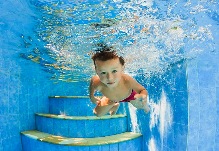 Boy in red bathers swimming underwater without goggles.