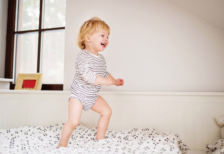 Smiling toddler jumps on a bed.