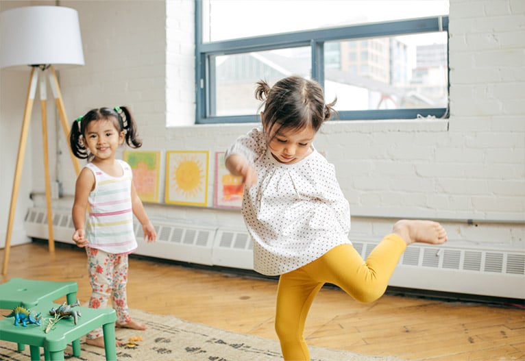 Two toddler girls dancing in a living room.