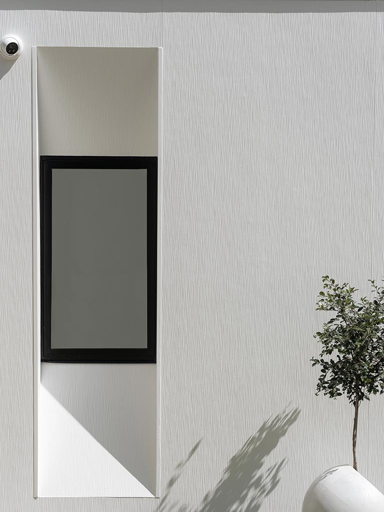 White external wall of a modern house with a black window.