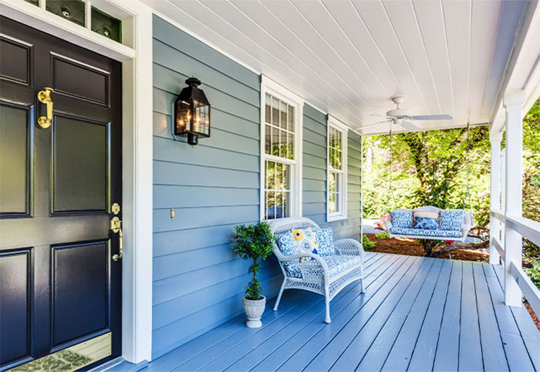 Verandah of a blue weatherboard house with a black front door.