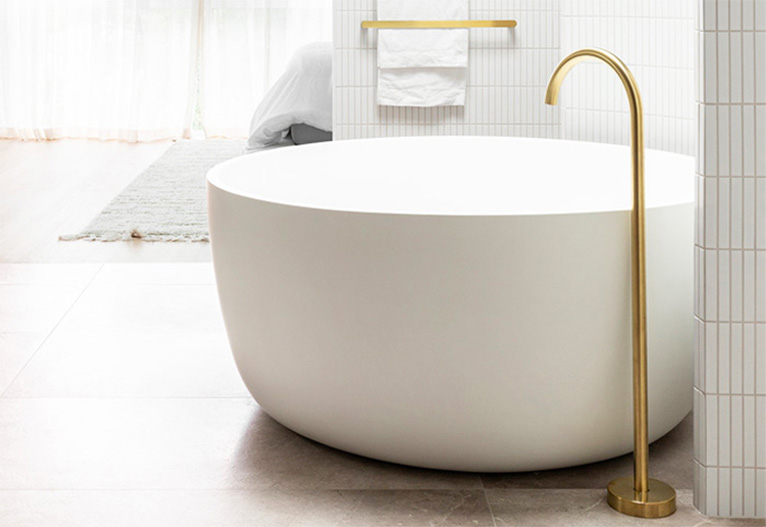 Brushed gold bath tap next to a round tub.