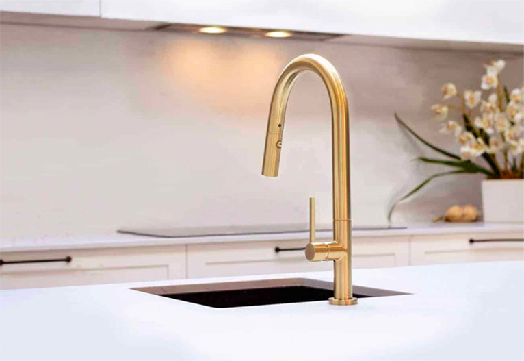 Brushed brass mixer tap mounted on a white bench in a modern kitchen.