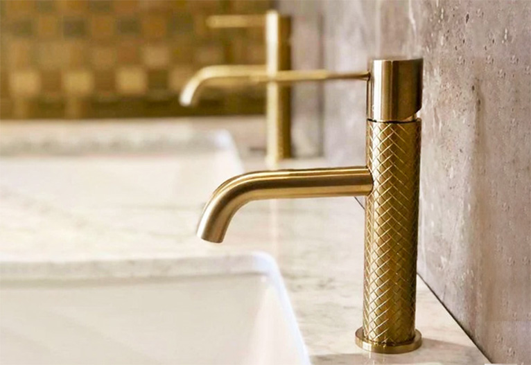Brushed brass taps mounted on white stone bench.