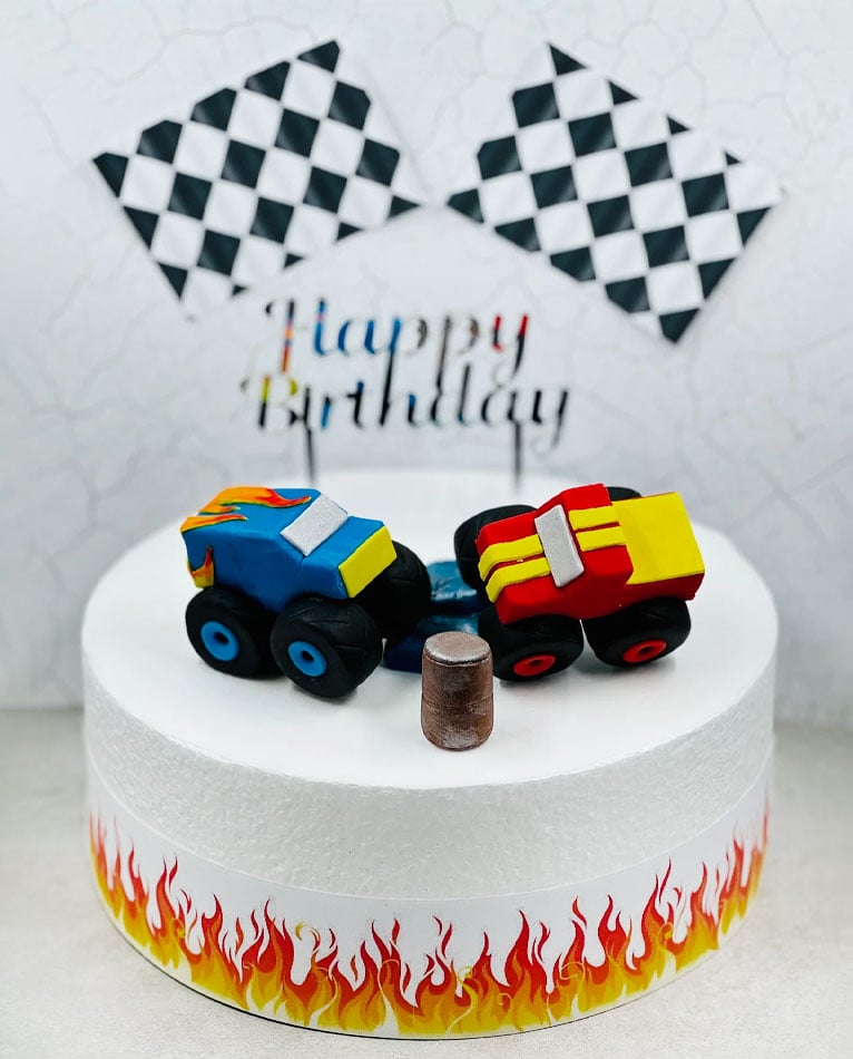 Fondant trucks on top of a white birthday cake.