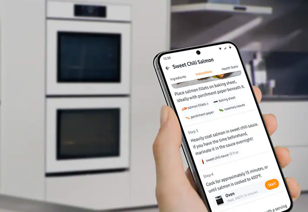 Close up of person reading a recipe off a phone in front of an oven.