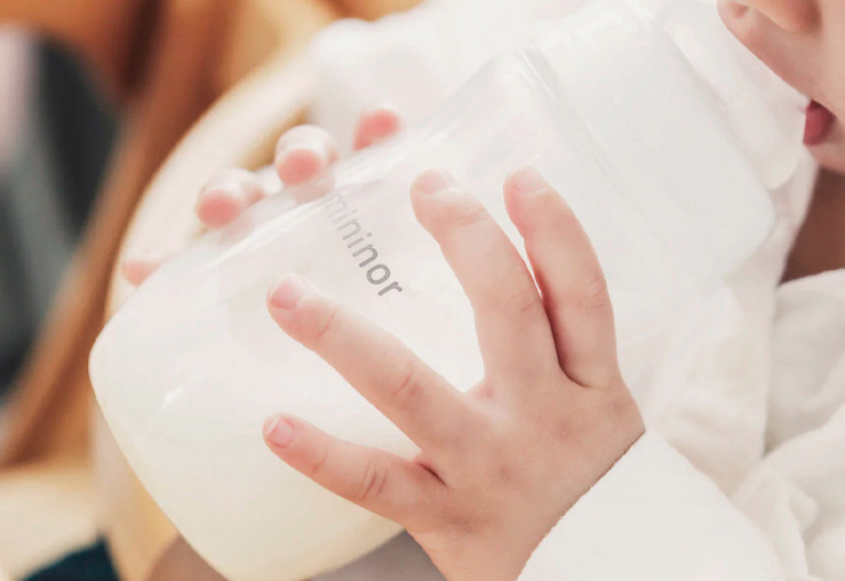Baby holding a mininor glass feeding bottle.
