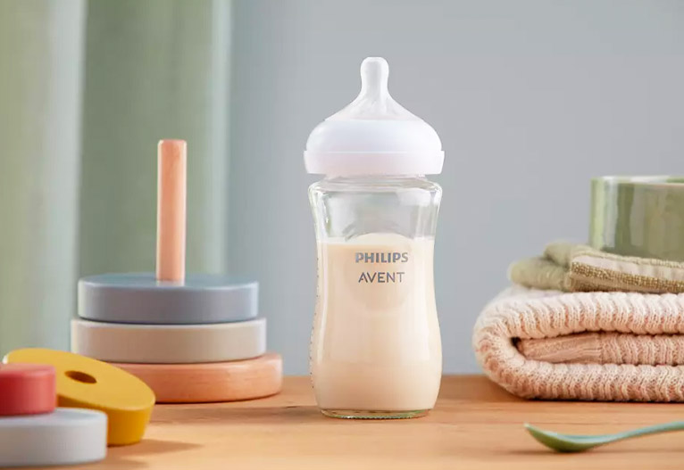 Philips Avent glass baby bottle on a table next to baby toys.