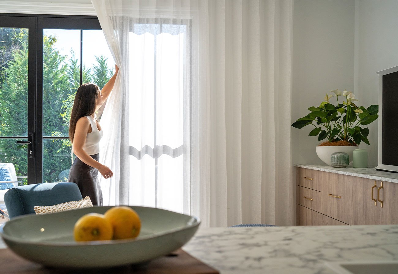 Opening white sheer curtains in apartment living room.