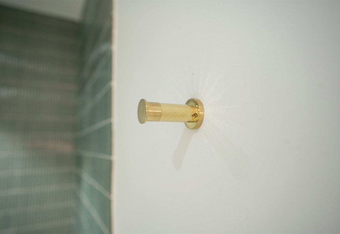 Brushed brass robe hook mounted on a white bathroom wall.