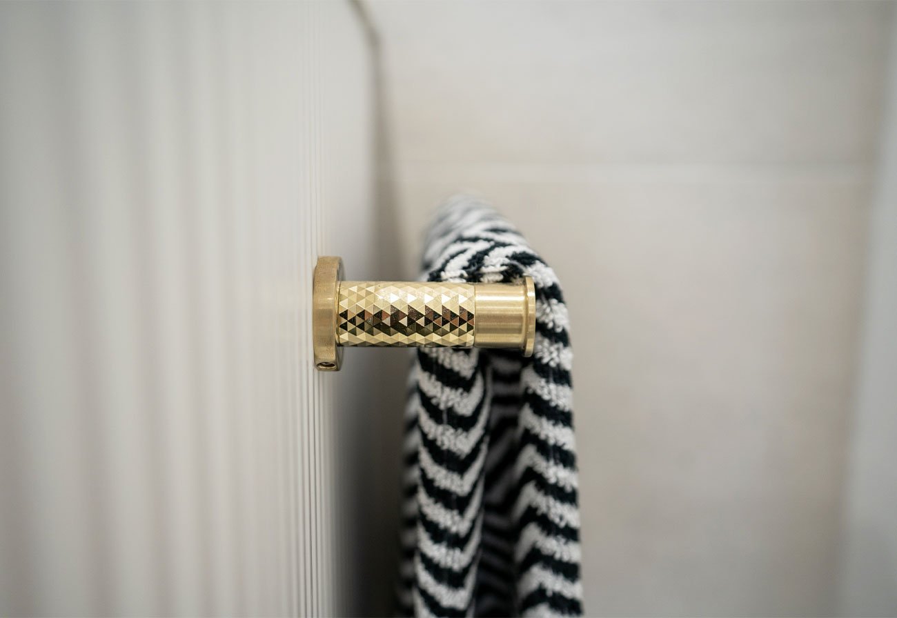 Side of a brushed brass towel rain with a black and white towel hung over it.