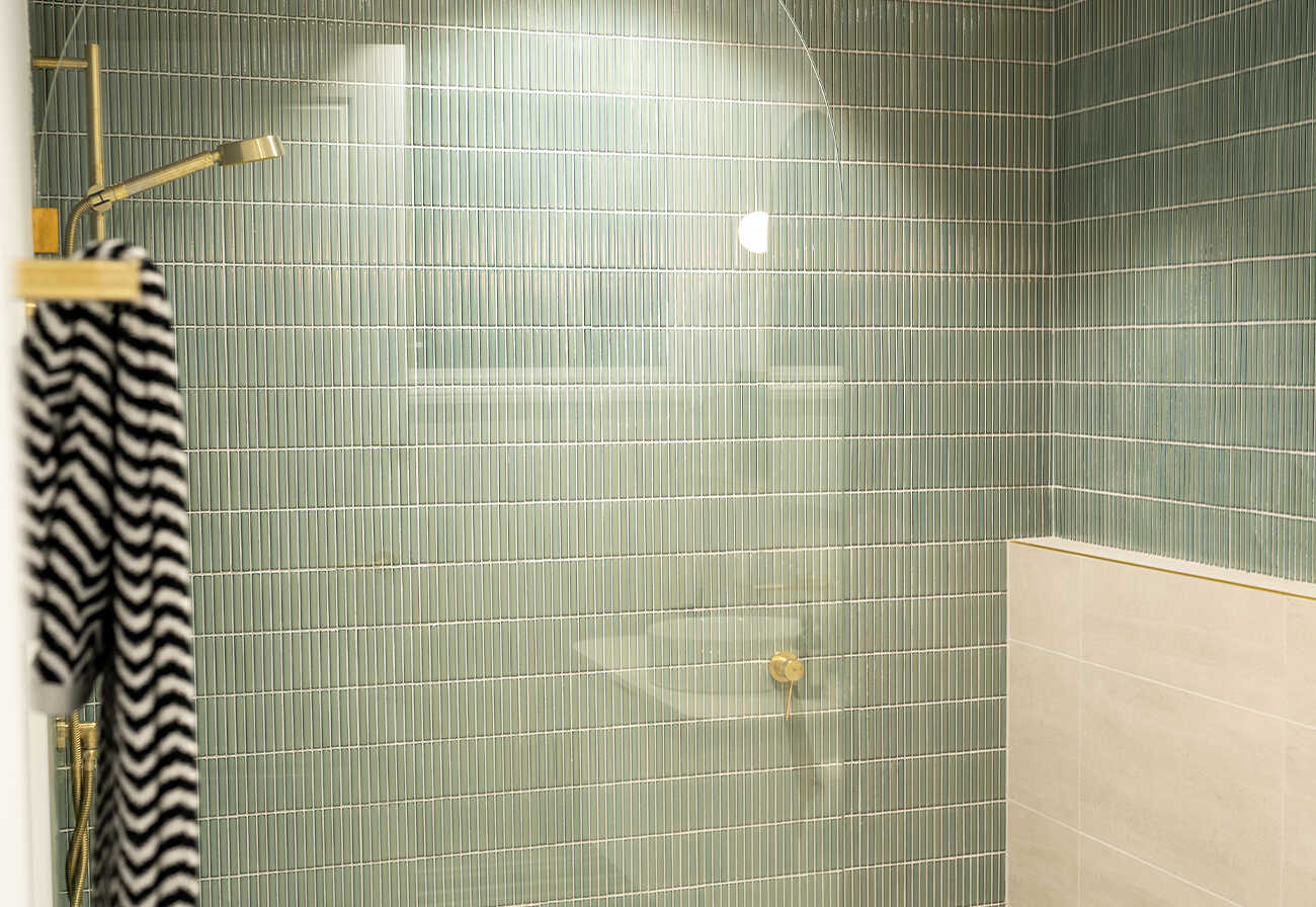 Shower cubicle with brushed brass taps and sage green tiles.