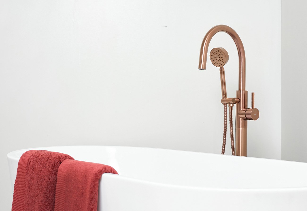 Brushed copper freestanding tap behind a white bath.