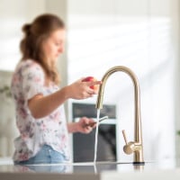 Woman touching kitchen tap to turn it off.