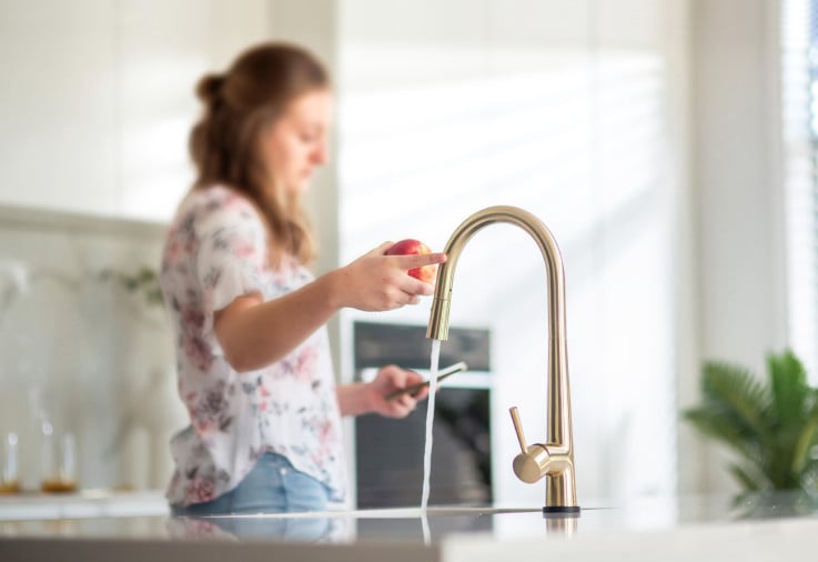 Woman touching kitchen tap to turn it off.