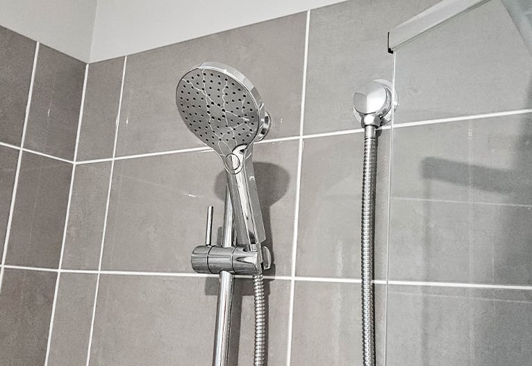 The Greens BubbleJet shower head in a grey tiled shower cubicle.