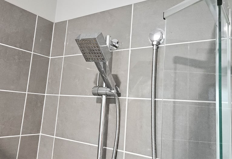 Square shower head in a grey tiled shower cubicle.