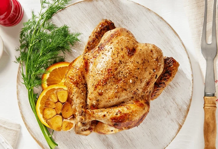 Hot roast chicken on a plate with roasted garlic.