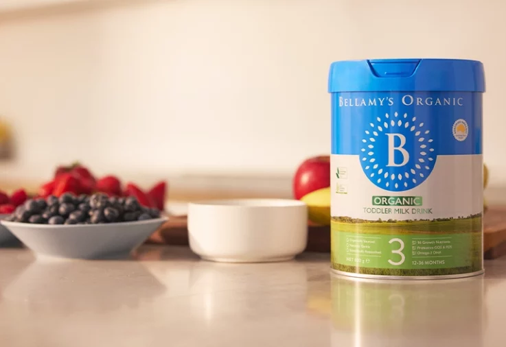 Bellamy's Step 3 Toddler Milk Drink on a bench next to bowls of fruit.