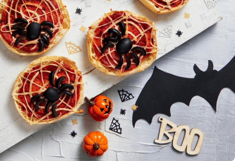 Spider pizzas on a bench with Halloween decorations.