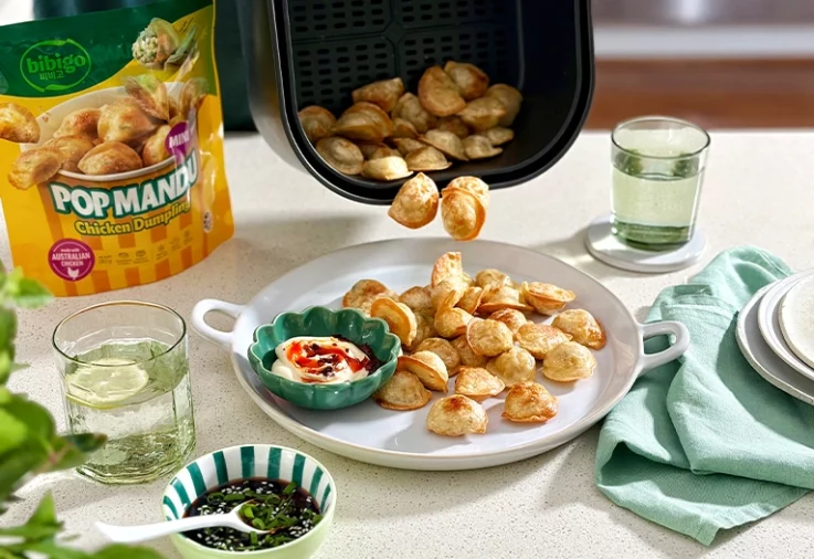 Bibigo Mini Pop Mandu chicken dumplings tipped from an air fryer onto a plate, with dipping sauces.